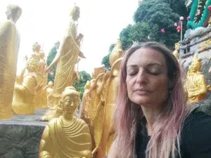 En un templo budista, rodeada de figuras doradas de monjes y una mujer en primer plano, con los ojos cerrados, meditando