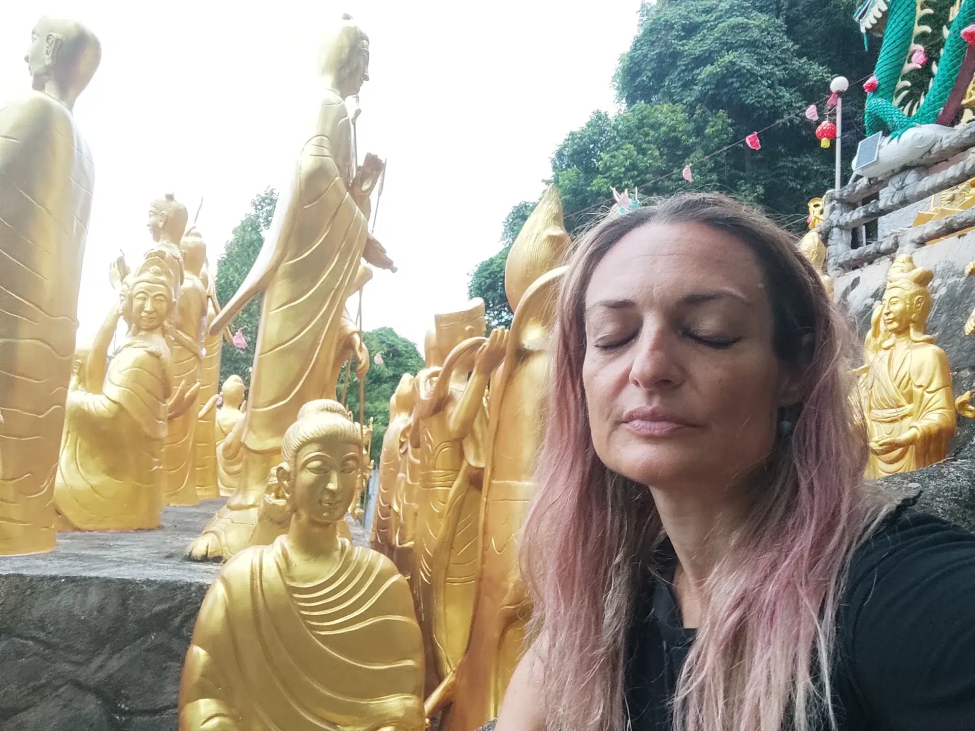 En un templo budista, rodeada de figuras doradas de monjes y una mujer en primer plano, con los ojos cerrados, meditando