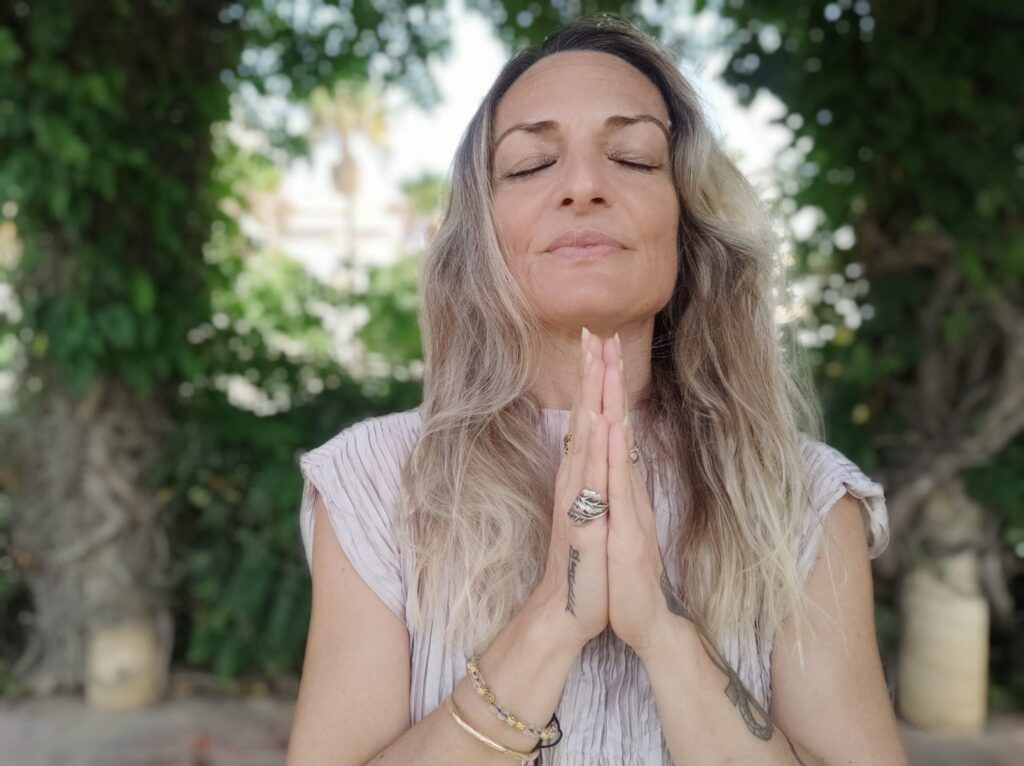 Mujer con gesto de manos haciendo Namasté y ojos cerrado con expresión de calma, paz, serenidad y sonrisa.