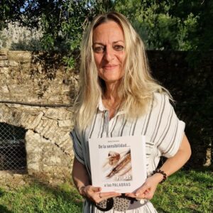 Jenny Carrasco, autora, sosteniendo su poemario De la sensibilidad a las palabras en un entorno natural.